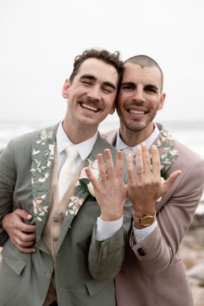 a LGBTQ couple smiling and showing off their wedding rings